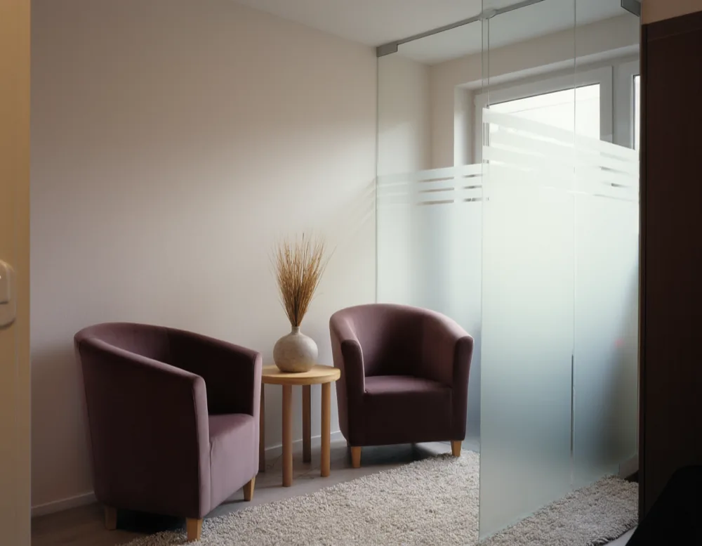 The waiting corner: two plum armchairs either side of a small oak table behind a frosted glass partition.